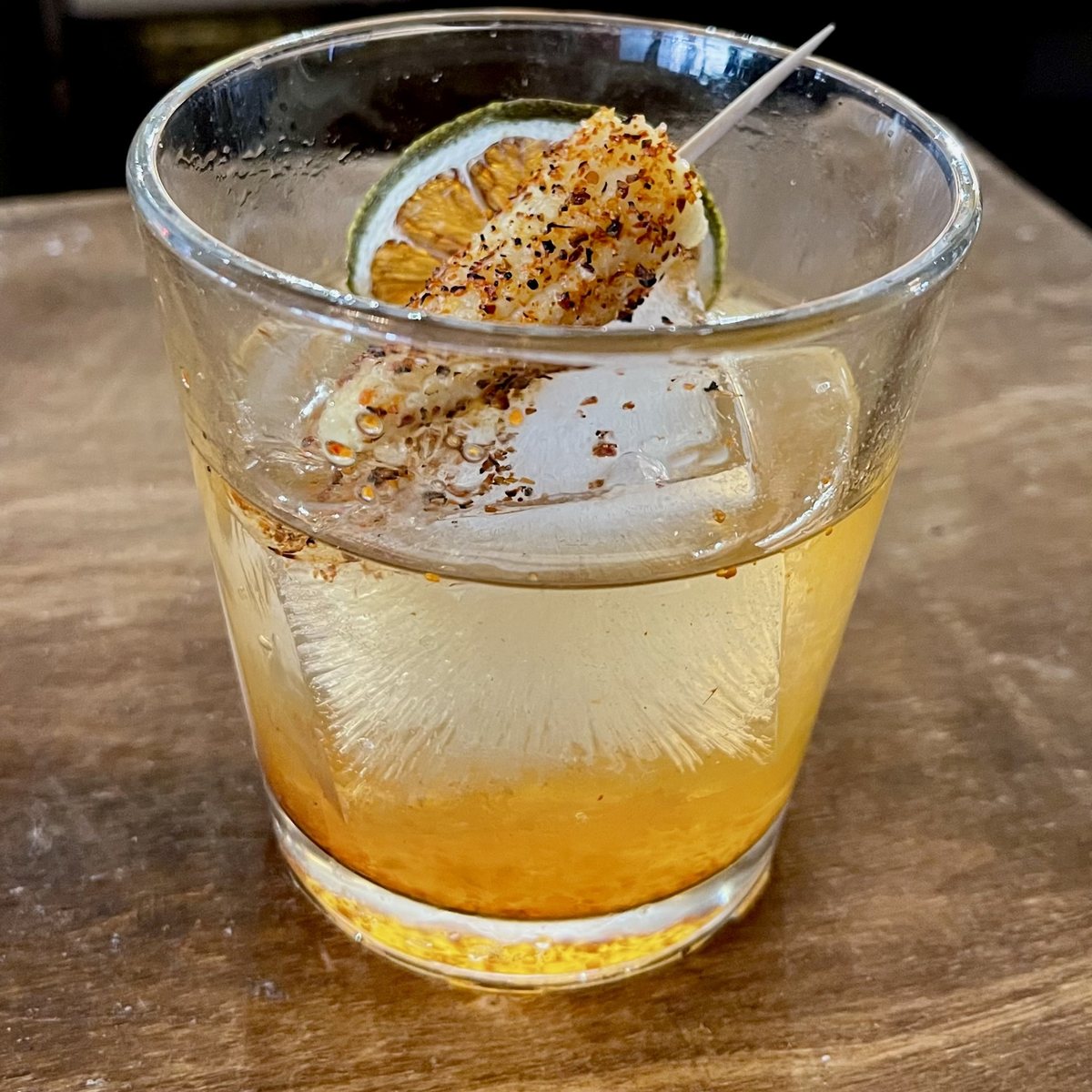 The Corn Fed Cowboy at the Alcove Social bar: a rocks glass over a large ice cube, garnished with a lime wheel and baby corn rolled in Tajin